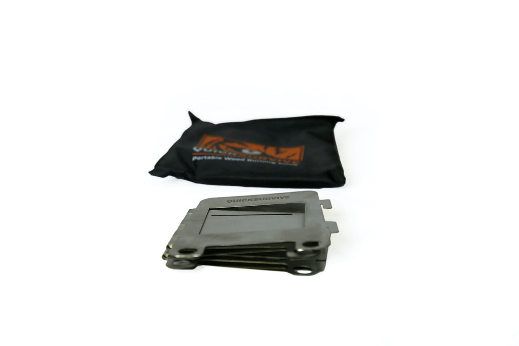 A compact, folded metal stove lies on a white surface with a black carrying pouch in the background. The pouch has an orange design and text that includes the word "QUICKSURVIVE," hinting at the Portable Mini Foldable Wood Burning Survival Stove by QUICKSURVIVE—a perfect addition to survival packs or as a portable camping stove.