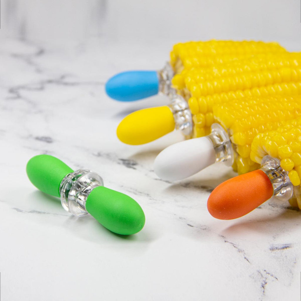 A group of Grand Fusion Housewares, LLC Corn on the Cob Holders with Stainless Steel Prongs & Silicone Grips displayed on a marble table at the XSpecial Marketplace.