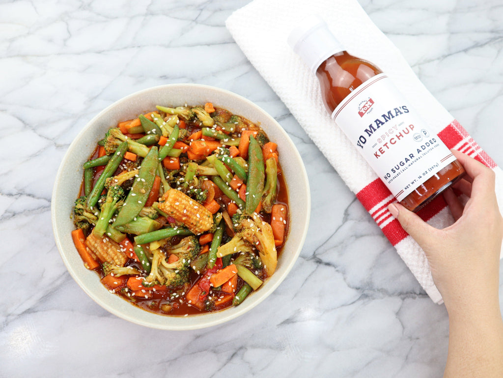 A XSpecial Foodie holding a bowl of vegetables next to a bottle of Spicy Ketchup (Keto and Paleo Certified) by Yo Mama's Foods.