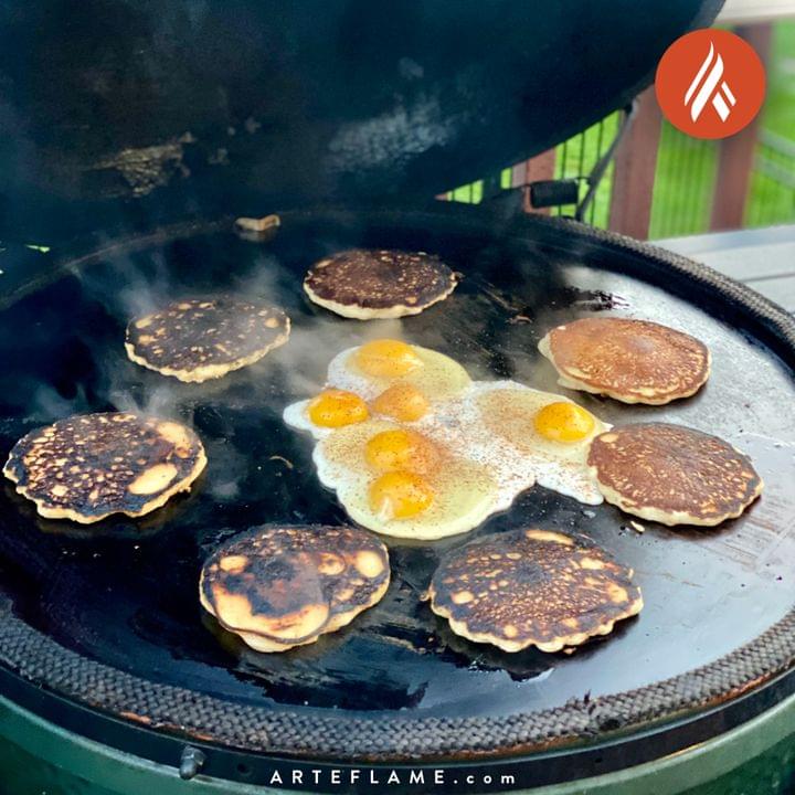 Green Egg Style / Kamado Style Solid Plancha Griddle Insert by Arteflame Outdoor Grills are being cooked on a grill using the Blade Meat Tenderizer Tool.