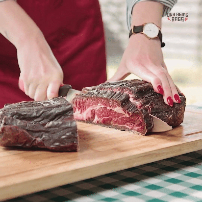 A woman using a Meat Tenderizer Tool cuts a piece of steak on a Large DryAgingBags™ by DryAgingBags™ for Foodies and Meat Lovers.