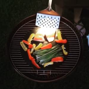 A person using a LED Spatula from Grillight.com to cook vegetables on a grill.