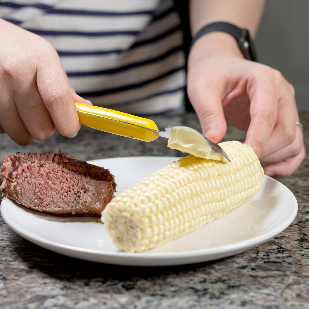 A person is slicing a piece of Grand Fusion Housewares, LLC's Corn Holder 5pc Set plus Butter Once 2pk, (BUNDLE) using a Meat Tenderizer Tool.