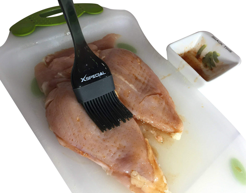 A chicken breast on a cutting board being flipped with a XSpecial Black Basting Brush.