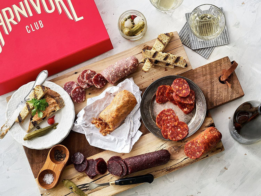 A carnivore's dream: a variety of meats packaged in a Carnivore Club Classic Box Sampler, accompanied by a wooden cutting board from Carnivore Club USA.