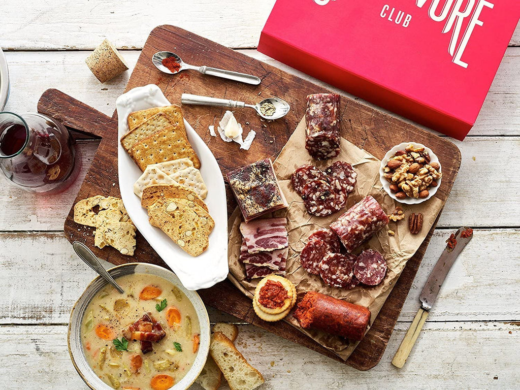 A tray of XSpecial Marketplace Carnivore Club Classic Box Sampler by Carnivore Club USA, bread and soup on a wooden cutting board.