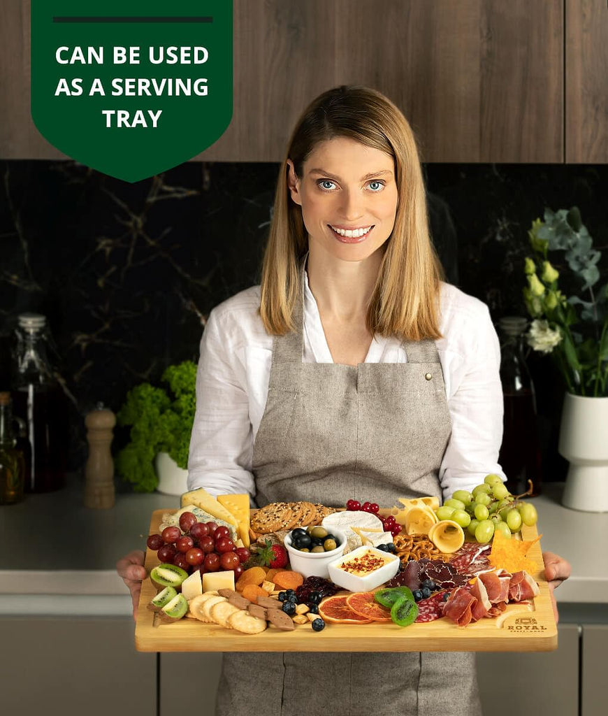 A foodie woman showcasing her love for XSpecial produce and meat by holding a Large Cutting Board, 20×14" by Royal Craft Wood adorned with an array of vibrant fruits and vegetables.
