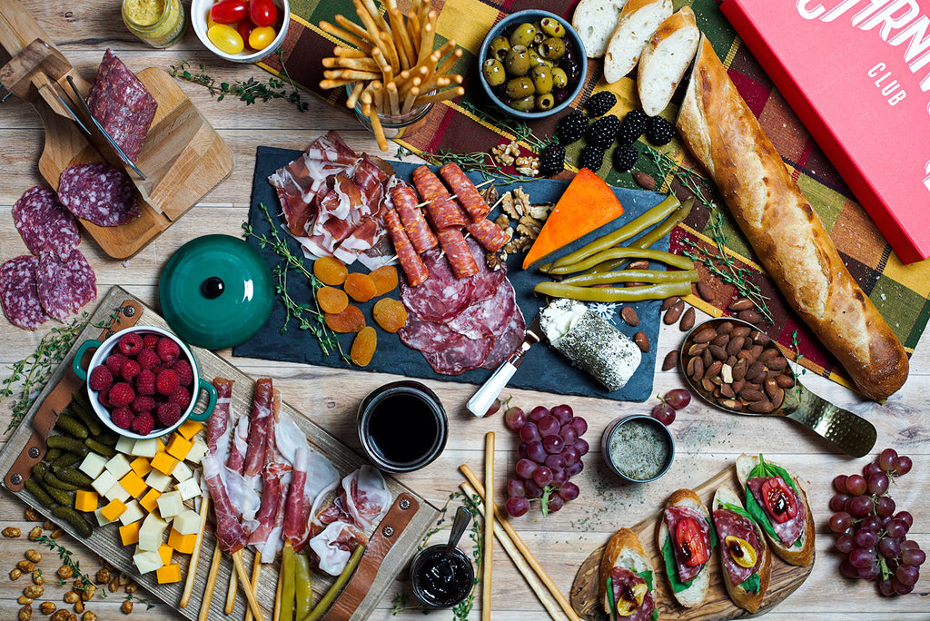 A variety of Classic Box Meats & Jams, Crackers, Cheese for Foodies by Carnivore Club USA are laid out on a wooden table, showcasing the Blade Meat Tenderizer Tool.