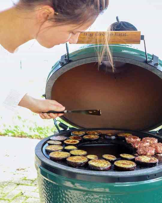 A woman is preparing XSpecial meat on an Arteflame Outdoor Grills Kamado Style Plancha Griddle.