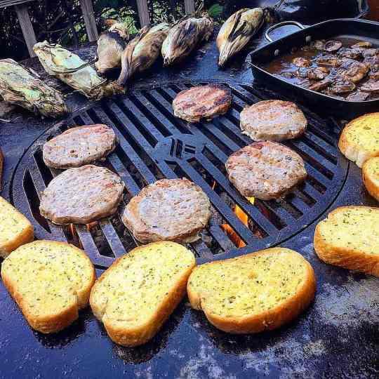 An Arteflame Outdoor Grills BBQ grill with burgers and bread on its Kamado Style Plancha Griddle and Grill Grate Combination Insert appeals to foodies.