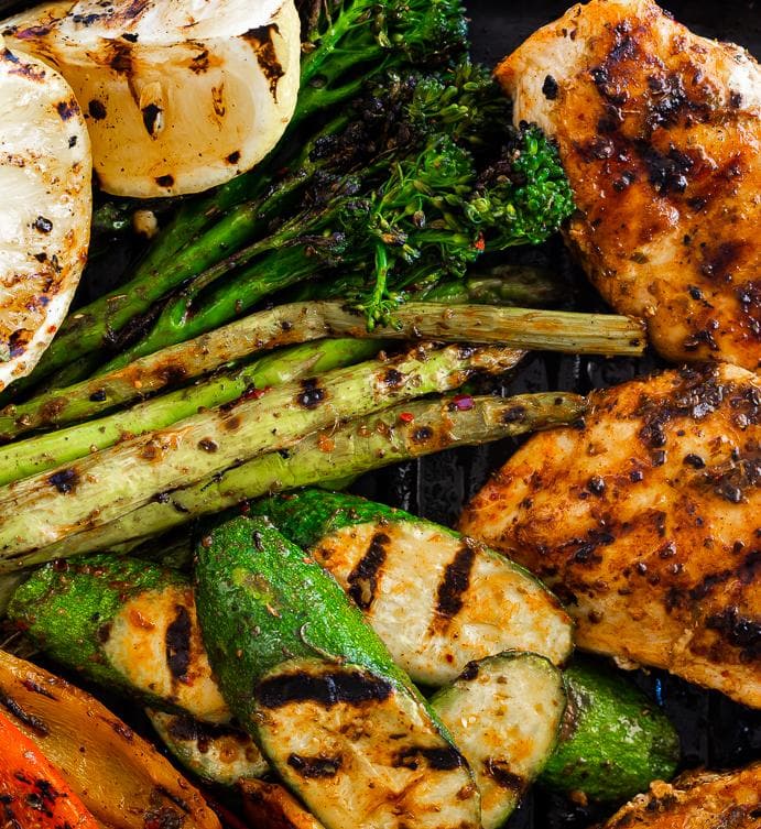 Grilled chicken and vegetables on an Arteflame Outdoor Grills' Griddle / Plancha Insert for Gas, Electric with Blade Meat Tenderizer Tool.