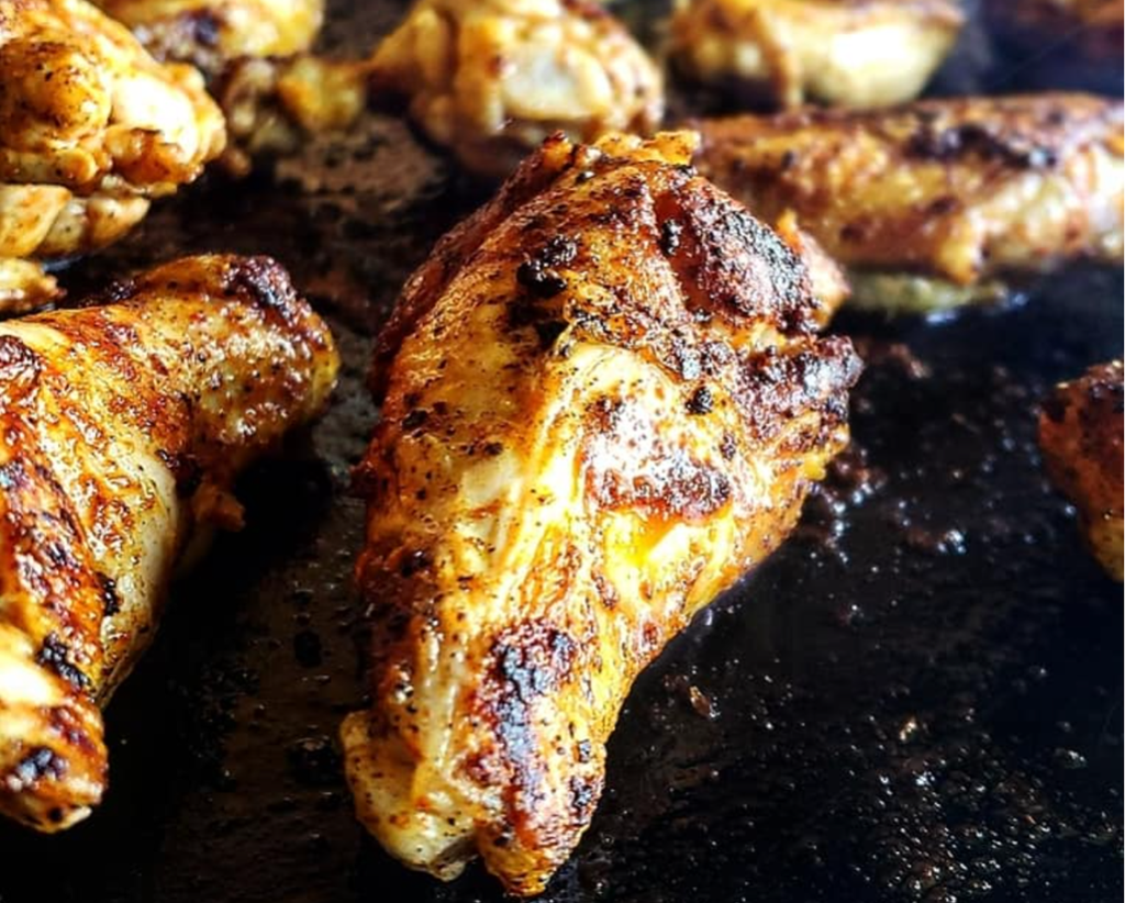 Grilled chicken wings on an Arteflame Outdoor Grills Griddle enhanced with a Meat Tenderizer Tool.