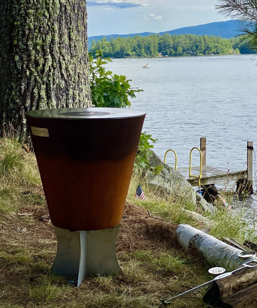 An Arteflame One Series 20" Grill, perfect for Meat Lovers and Foodies, grilling on the grass next to a body of water.