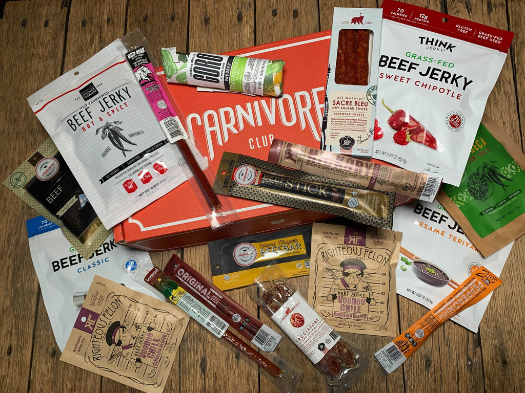 A Mega Meat Box - Minimum 18 Items by Carnivore Club USA of various foods and snacks on a wooden table, perfect for Foodies who love trying new cuts and flavors, with the added