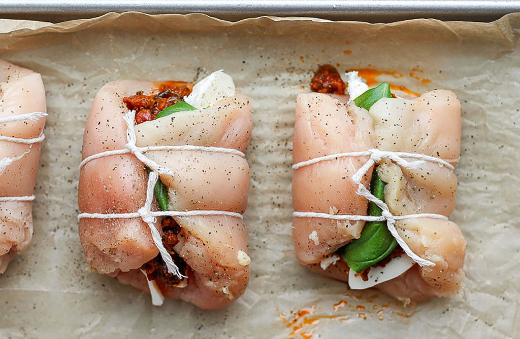 Stuffed chicken breasts wrapped in Regency Wraps Cotton Butchers Cooking Twine on a baking sheet.