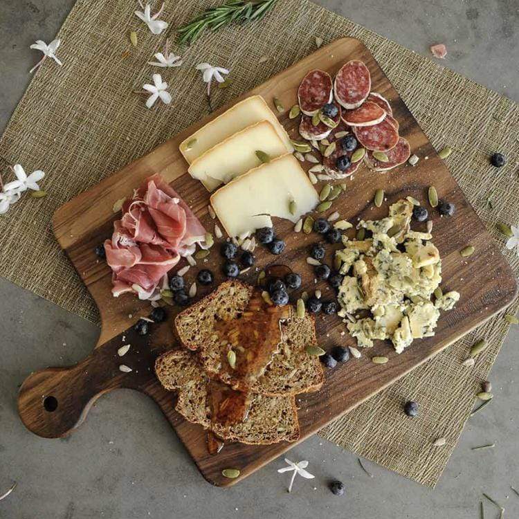 A Virginia Boys Kitchens' cutting board specially designed for meat lovers, featuring a knob handle and showcasing various meats and cheeses.